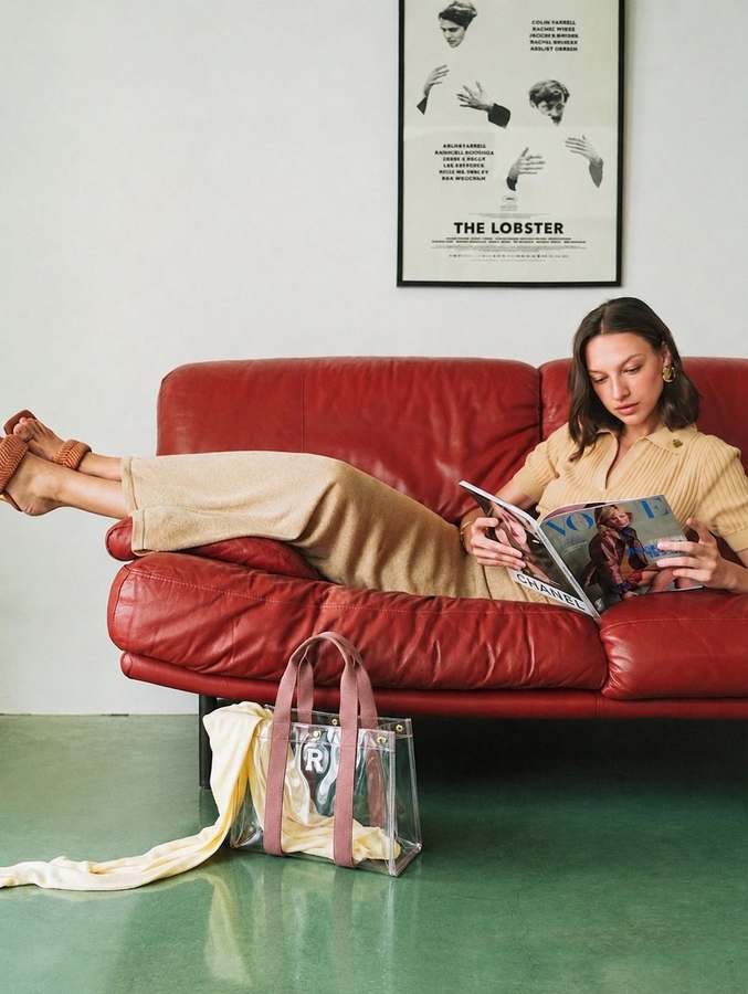 A customer relaxing on a red leather sofa with the clear Baganic tote bag and a cream cardigan
